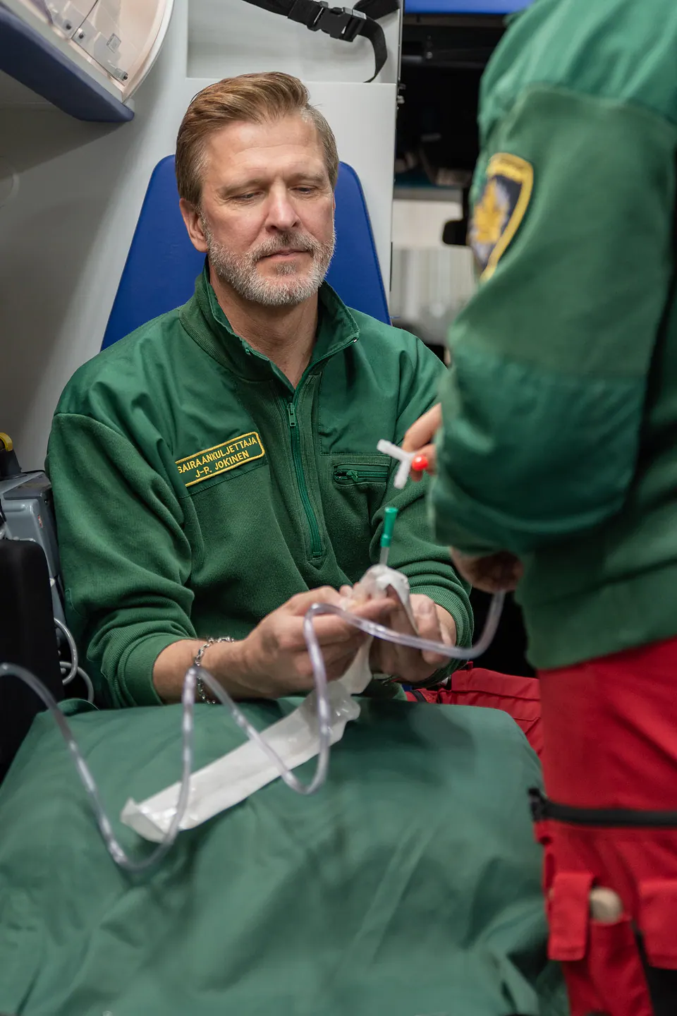 Varuste valmiiksi yhdessä Kaksi työntekijää käsittelee läpinäkyvää letkua ja pakkausta ambulanssin sisällä.