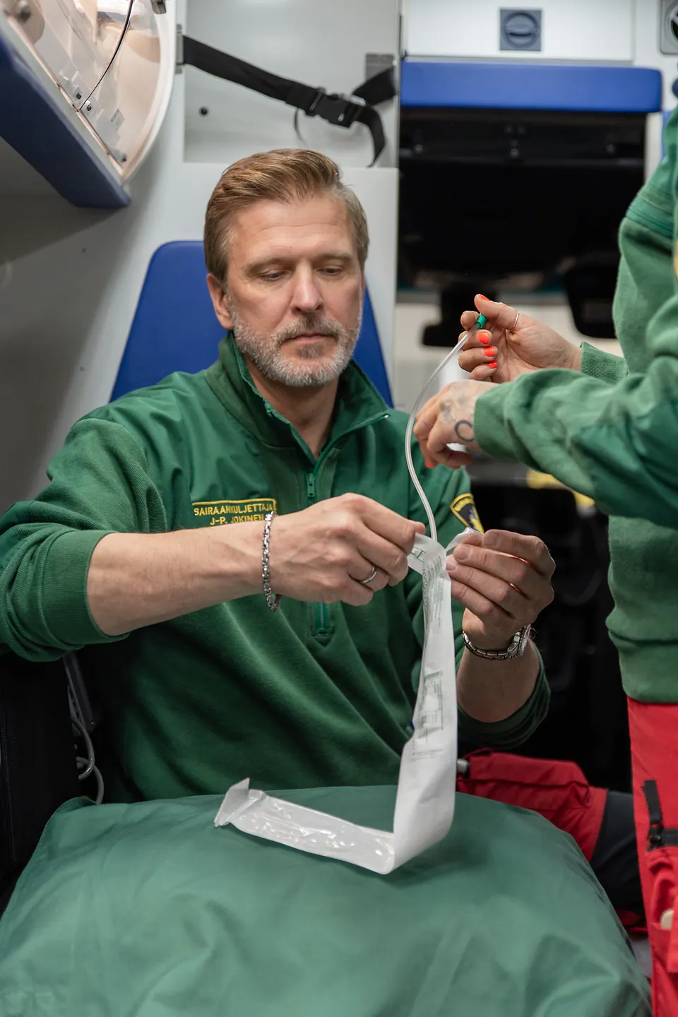 Valmistelu vaihe vaiheelta Kaksi työntekijää avaa pitkää pakkausta ja käsittelee läpinäkyvää letkua ambulanssin sisällä.