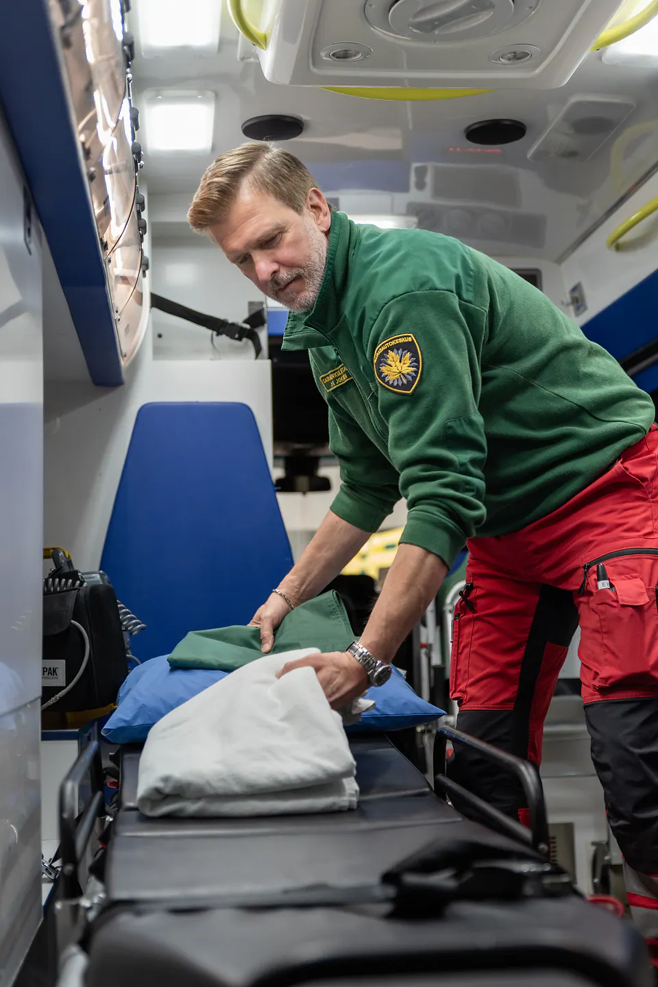 Viimeistely ennen lähtöä Työntekijä asettelee vaaleaa peitettä ja tyynyä paareille ambulanssin sisällä.