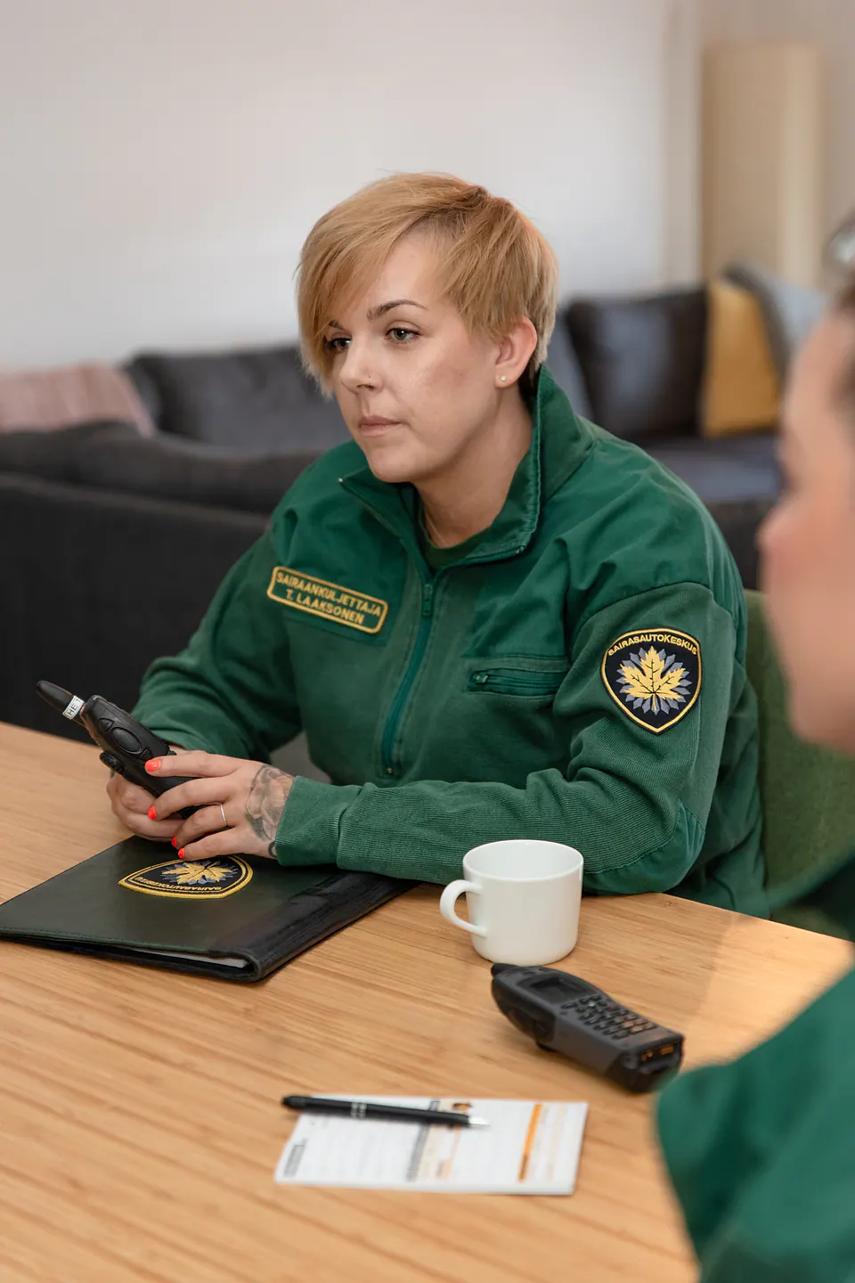 Valmiina kuuntelemaan Vihreään työasuun pukeutunut työntekijä istuu palaveripöydässä radiopuhelin käsissään.