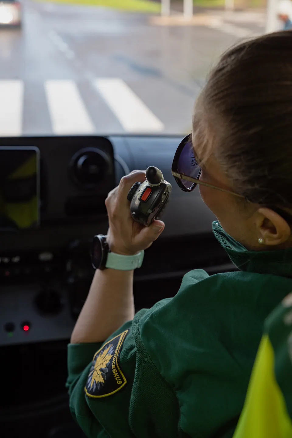 Viestintää matkalla Työntekijä käyttää radiopuhelinta ambulanssin etupenkillä suojatie edessään.