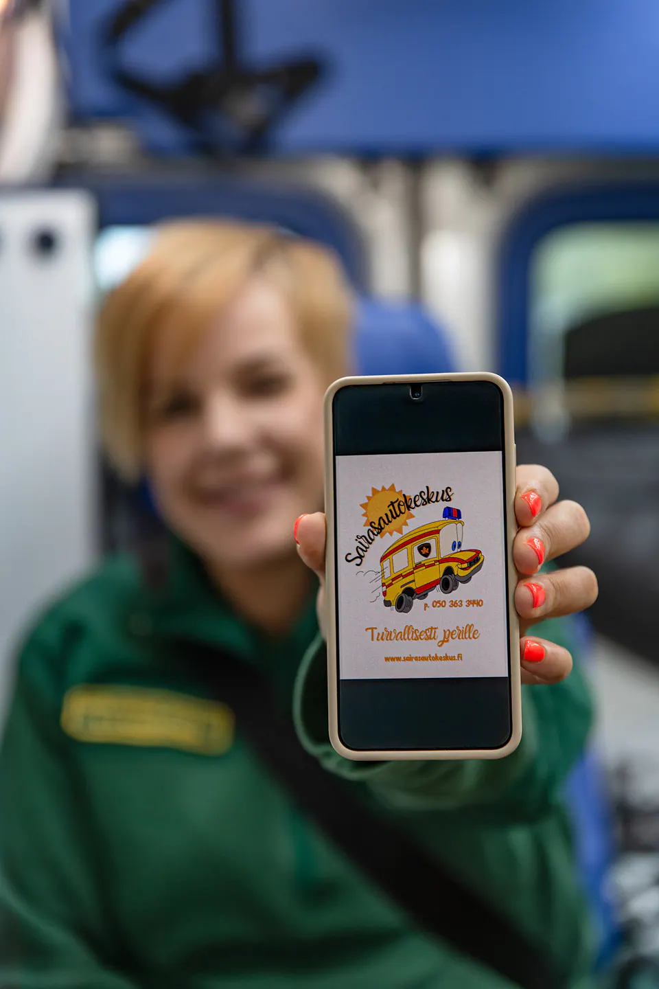 Tuttu tunnus puhelimessa Työntekijä näyttää puhelimen näytöllä Sairasautokeskuksen kuvitetun tunnuksen ambulanssin sisällä.