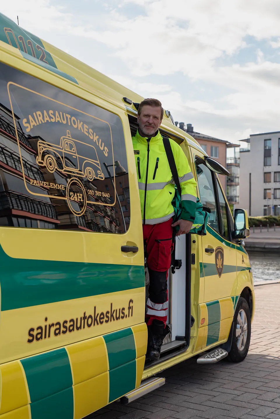 Matkaan varusteiden kanssa Työntekijä astuu ulos ambulanssin sivuovesta vihreä varustelaukku olallaan.