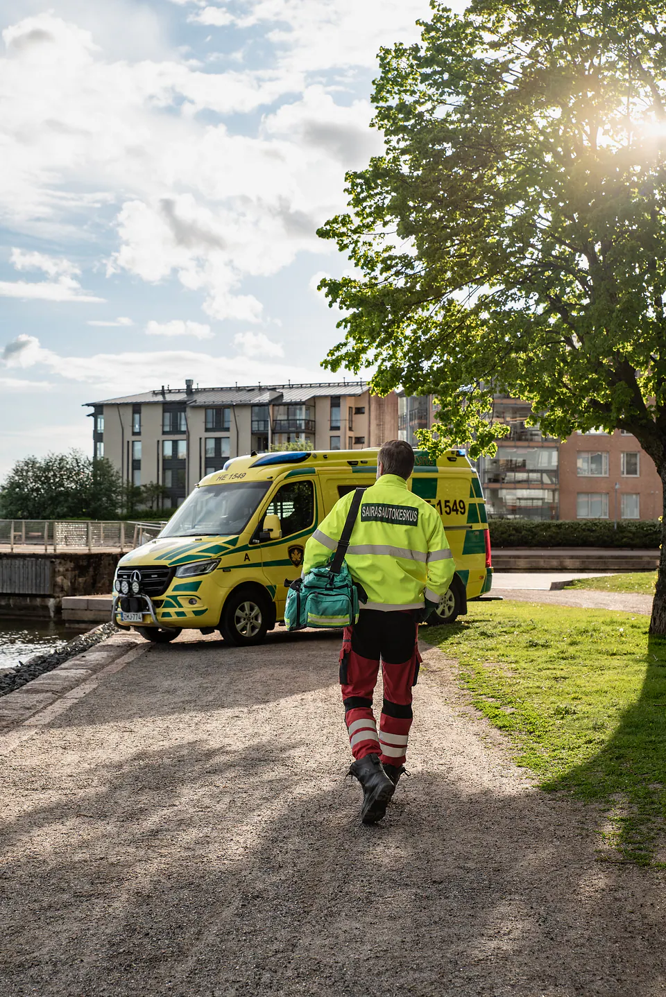 Matkalla autolle Työntekijä kävelee selin kameraan varustelaukku olallaan kohti ambulanssia ilta-auringossa.